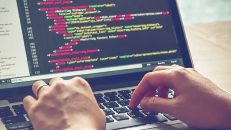 Hands typing on a laptop showing lines of website code